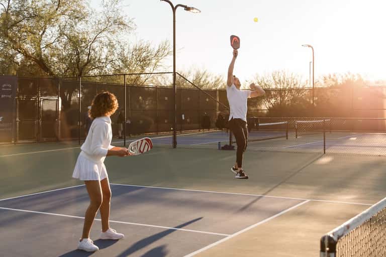 Female player serving during pickleball match on outdoor court at sunset