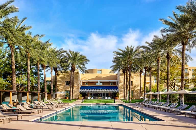 Resort lap pool with palm trees, lounge chairs, and modern building architecture