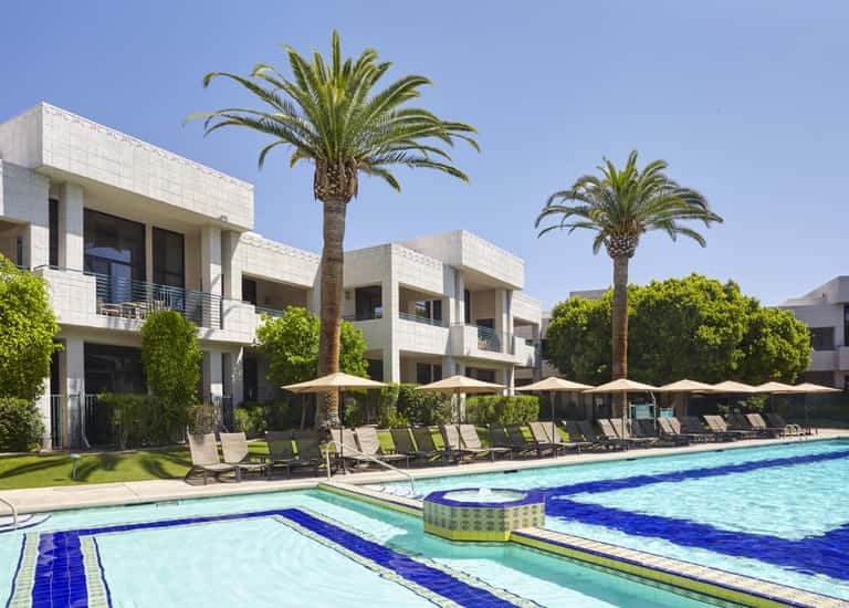 Resort swimming pool with lane markers, lounge chairs, palm trees, and modern white architecture