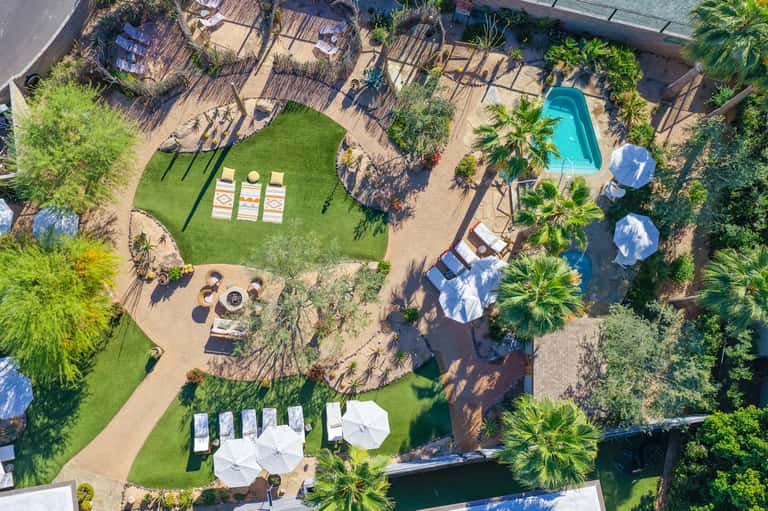 Aerial view of resort grounds with pool, manicured lawn, lounge areas, umbrellas, and desert landscaping