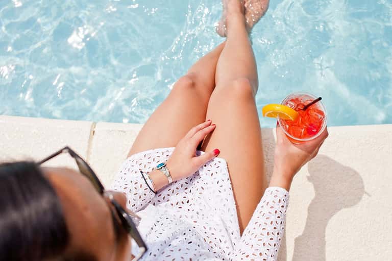 Woman's legs by pool holding tropical cocktail with orange slice
