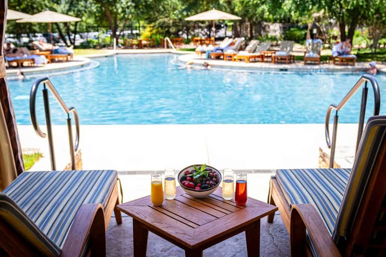 Poolside lounge seating with striped cushions, tropical drinks, and expansive pool view with umbrellas