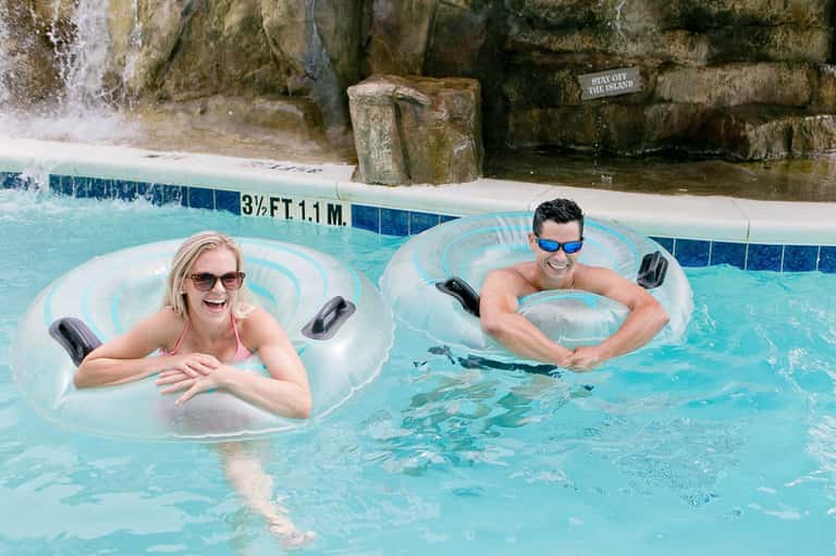 Two guests floating on inflatable tubes in a turquoise thermal pool with rock formations