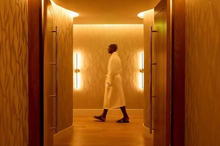 Modern hotel corridor with warm wood paneling and LED lighting, guest walking through hallway