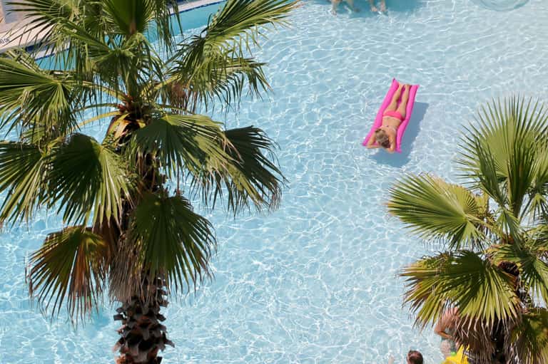 Aerial view of resort pool with person on pink float surrounded by palm trees