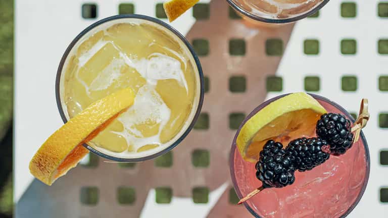 Overhead view of two vibrant cocktails: yellow citrus drink and pink berry cocktail with garnish