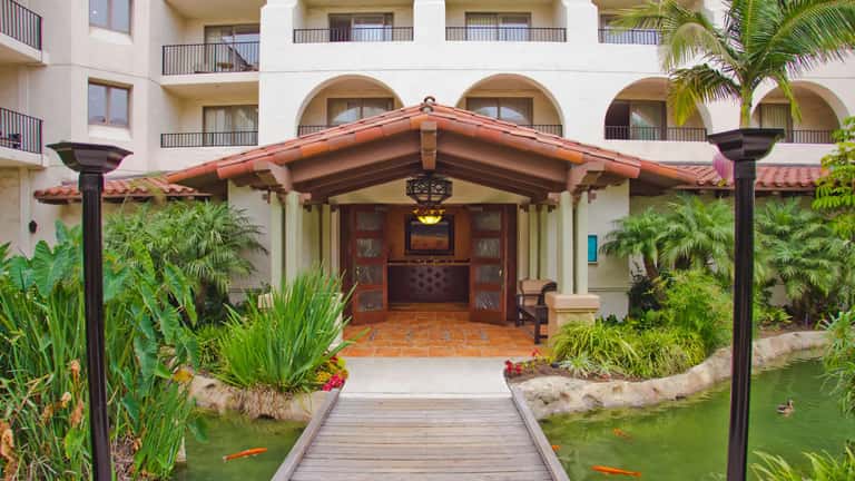 Resort entrance with Spanish colonial architecture, red tile roof, tropical landscaping, and koi pond