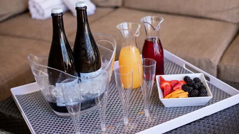 Luxury in-room beverage service with champagne, juices, fresh fruit platter on woven tray