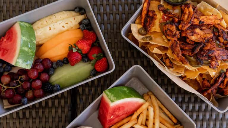 Room service food trays with fresh fruit, cheese, watermelon, bacon, chips, and appetizers