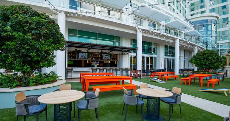 Modern outdoor courtyard with bright orange picnic tables, green lawn, and contemporary bar