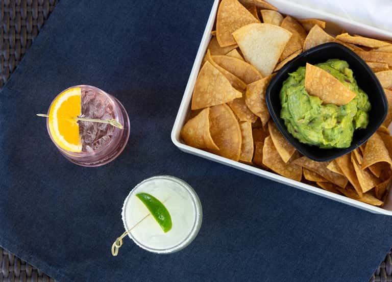 Cocktails and guacamole with tortilla chips on a dark blue outdoor table setting
