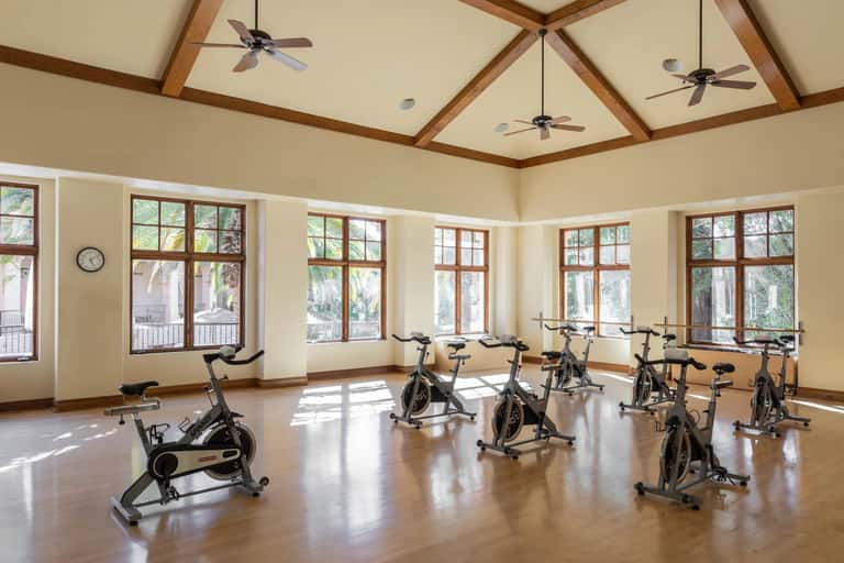 Bright fitness studio with wooden beams, multiple exercise bikes, and large windows overlooking grounds