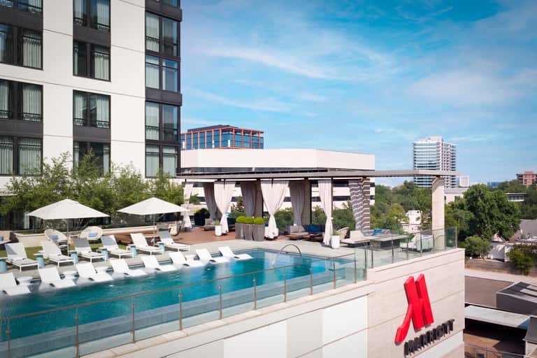Luxury rooftop pool with lounge chairs, white umbrellas, pergola, and city skyline in background