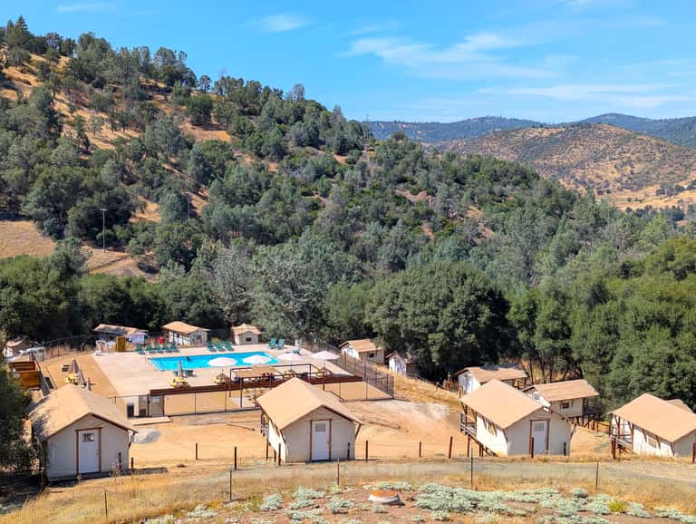 Aerial view of glamping resort with pool, cabins, and forested hillside landscape