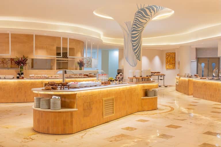 Luxury hotel buffet restaurant with wooden curved counters, zebra artwork, ambient ceiling lights, and marble flooring