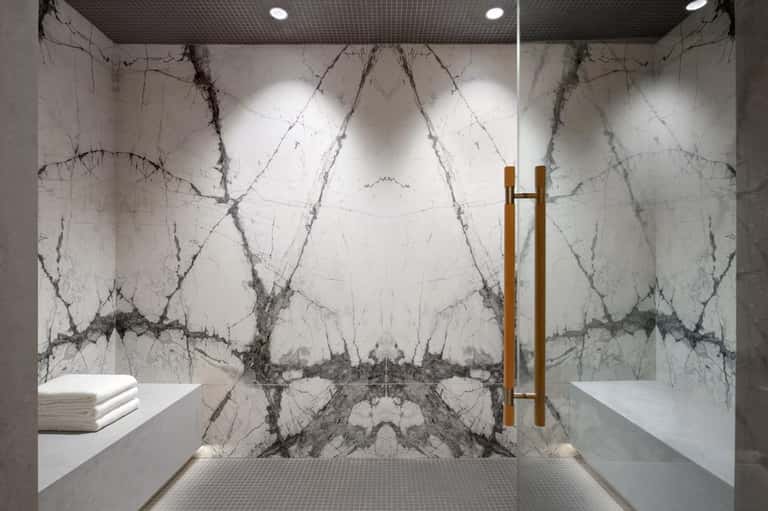 Luxury marble steam shower with symmetrical design, gold fixtures, and heated stone benches