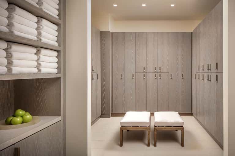 Spa changing room with light wood lockers, rolled white towels, wooden benches with white cushions, and green apples
