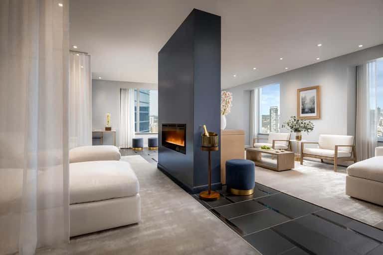 Contemporary suite with fireplace, dark accent wall, cream seating, wooden furniture, and expansive city views