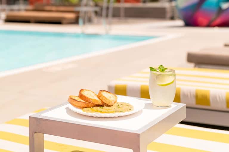 Poolside food service with appetizers and lime-garnished cocktail on striped lounge chair