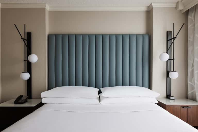 Modern hotel bedroom with teal upholstered headboard, white pillows, and contemporary black bedside lamps