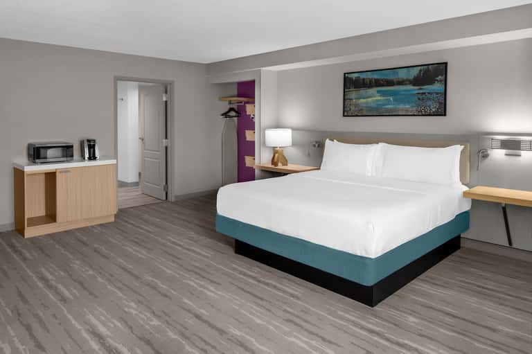 Hotel guest room with teal bed, wood accents, gray walls, and landscape artwork