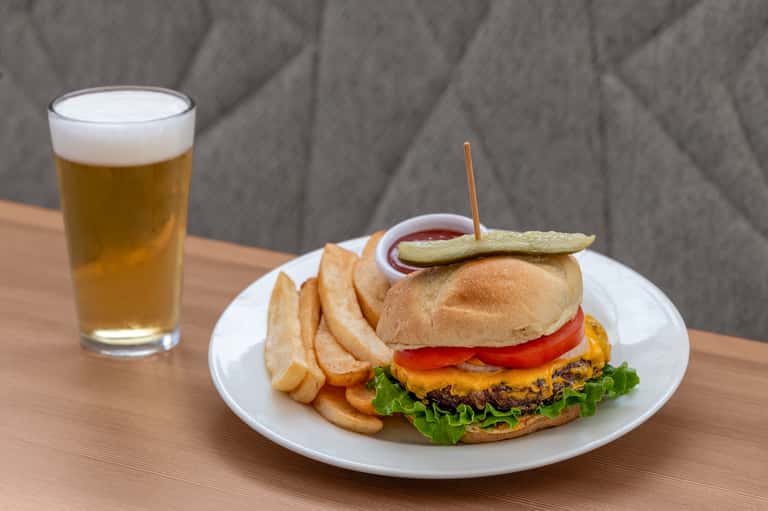 Burger and fries meal with beer on wooden table against gray textile background