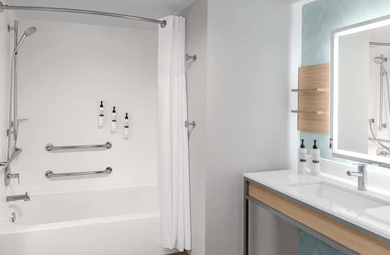 Modern bathroom with white shower surround, vanity with wooden accents, and lit mirror