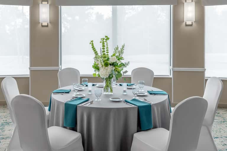 Elegant round dining table set for four with gray tablecloth, teal napkins, and floral centerpiece