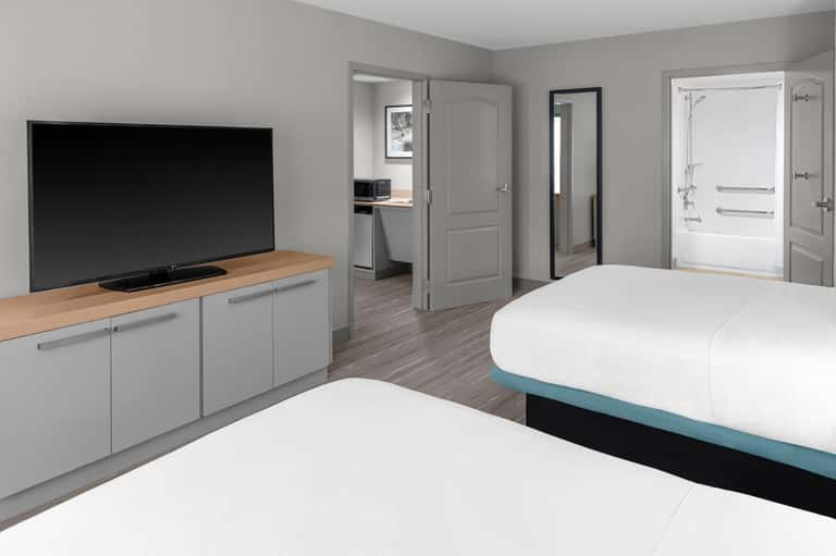 Modern hotel room with two queen beds, flat-screen TV, and ensuite bathroom with tub and shower