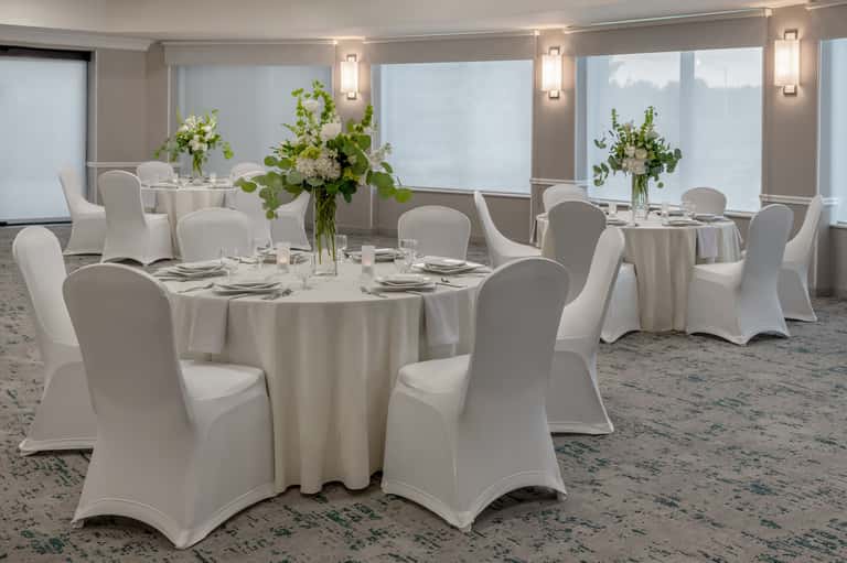 Elegant ballroom with multiple round tables set for events, white linens, and floral centerpieces