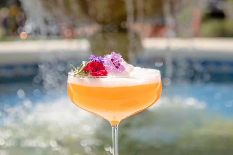 Elegant cocktail with orange liqueur and edible flowers by poolside