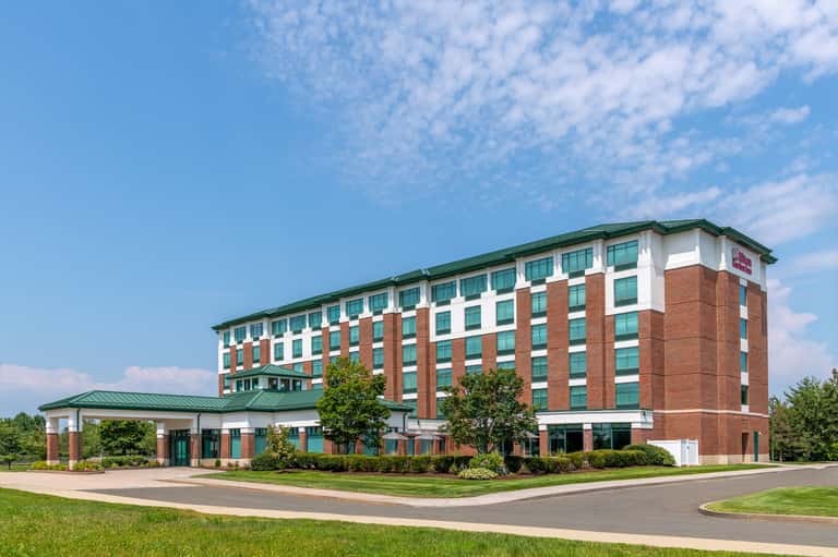Exterior of brick and white hotel building with green roof and manicured landscaping