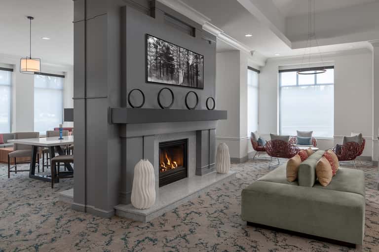 Modern lounge with fireplace, sofa seating, large windows, pendant lighting, and forest artwork