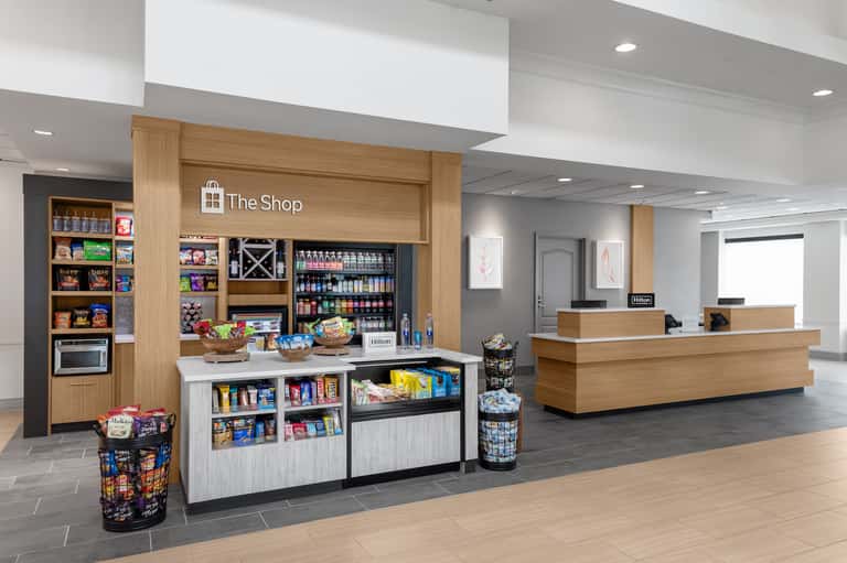 Hotel lobby with wooden reception desk, shop counter with snacks and beverages, and Hilton signage