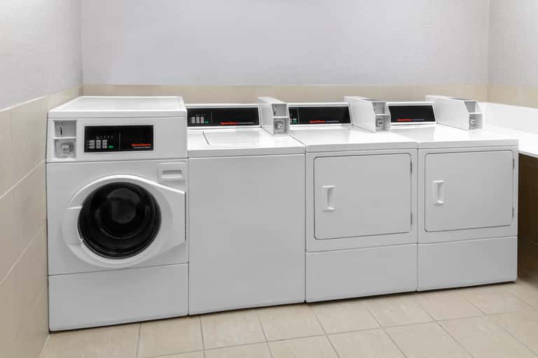 Commercial laundry room with washer, dryers, and folding counters in clean white and beige space