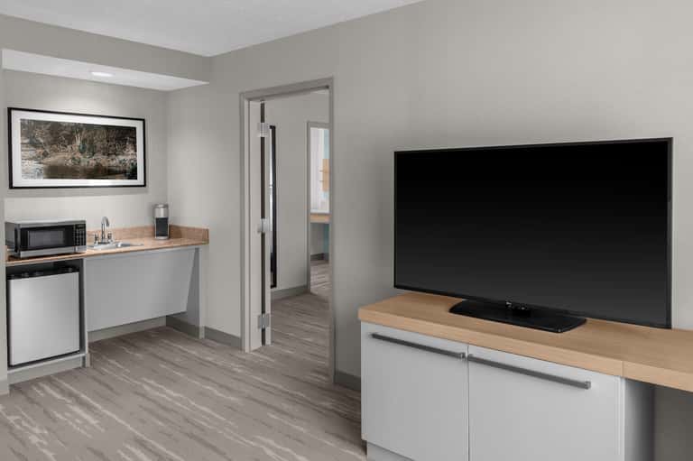 Hotel suite kitchenette with microwave, sink, and flat-screen TV mounted above wooden counter