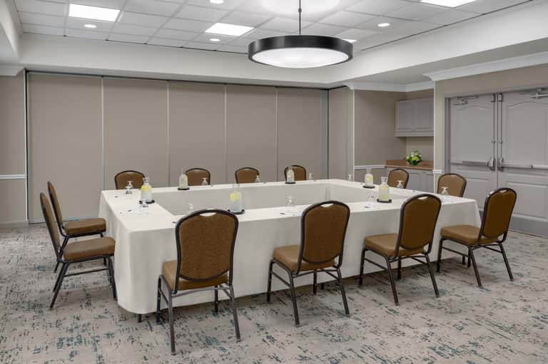 Meeting room with U-shaped white table setup, brown chairs, white cabinetry, and soft lighting