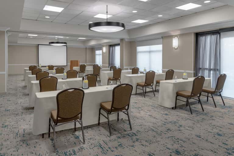 Large ballroom with multiple round tables, white linens, brown chairs, and projection screen