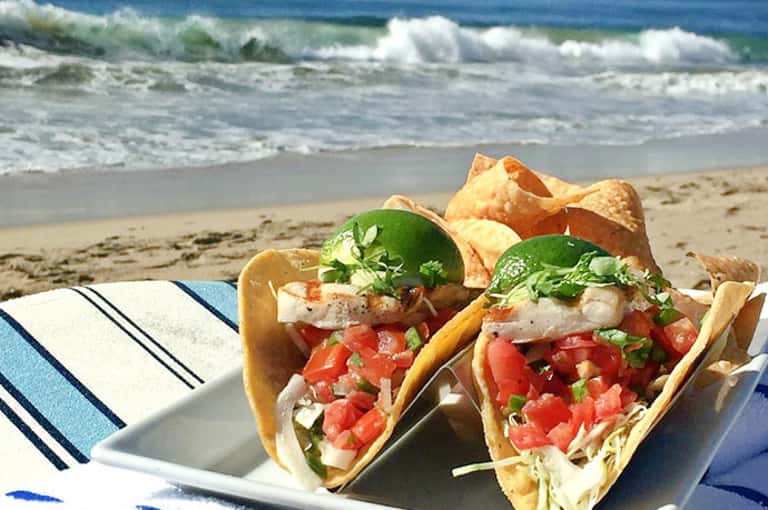 Fish tacos with fresh tomatoes and cilantro served beachside with ocean waves in background