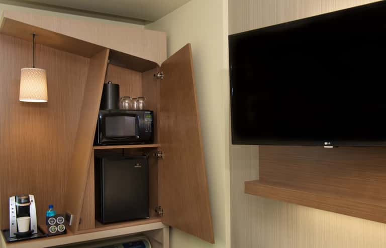 Hotel room closet and entertainment area with wooden cabinetry, flat-screen TV, microwave, and mini refrigerator