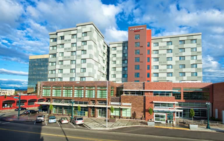 Courtyard by Marriott hotel exterior daytime view showing multi-story building with red accent tower, ground-level retail spaces, and parking