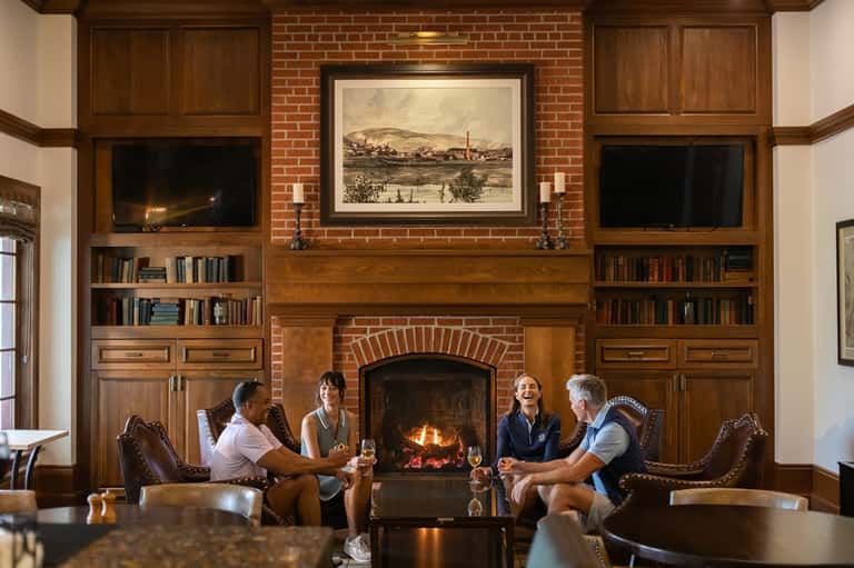 Group of people enjoying drinks by fireplace in elegant lounge with wood paneling and bookshelves