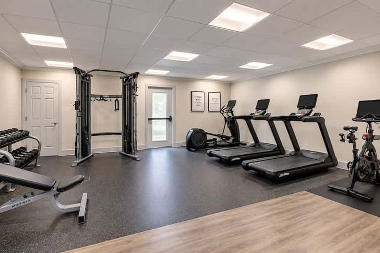 Fitness center featuring multiple treadmills, cable machine, dumbbells, and stationary bikes on dark flooring