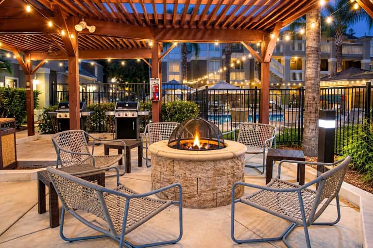 Evening patio with fire pit, lounge seating, pergola, grills, and ambient string lighting