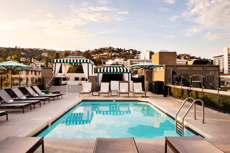 Rooftop pool with turquoise water, white cabanas with striped awnings, and city skyline views