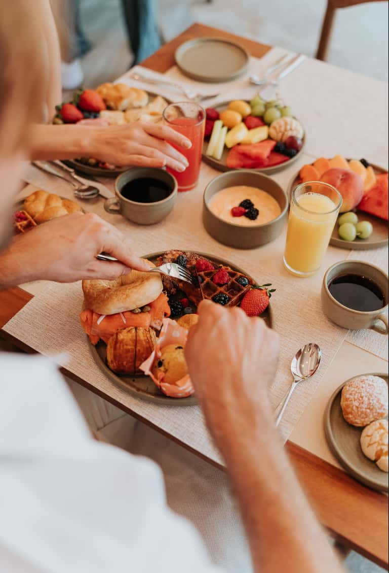 Couple enjoying breakfast with fresh fruits, pastries, juice, and coffee at a dining table