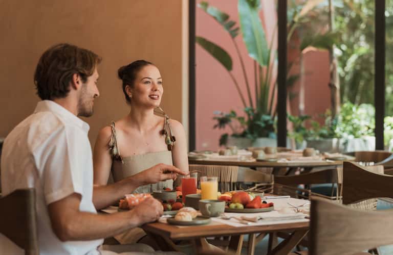Couple having drinks and fruit on a terrace overlooking a lush tropical garden courtyard