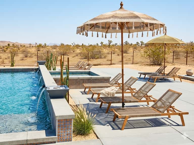 Desert resort pool with wooden loungers, large umbrellas, and desert landscape
