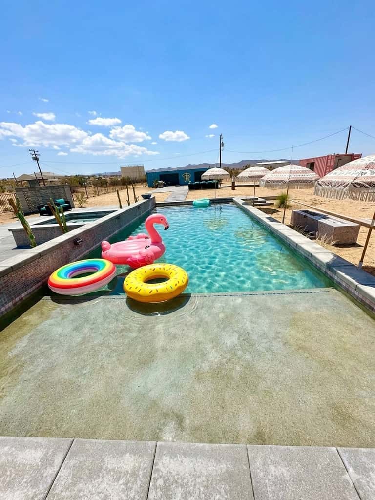 Resort pool with turquoise water, colorful floats, umbrellas, and desert mountain views