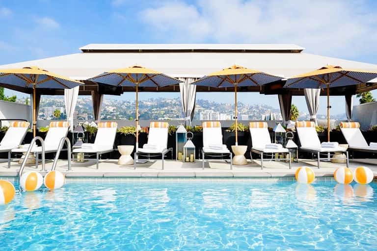 Luxury resort pool with yellow umbrellas, loungers, and city skyline view in background